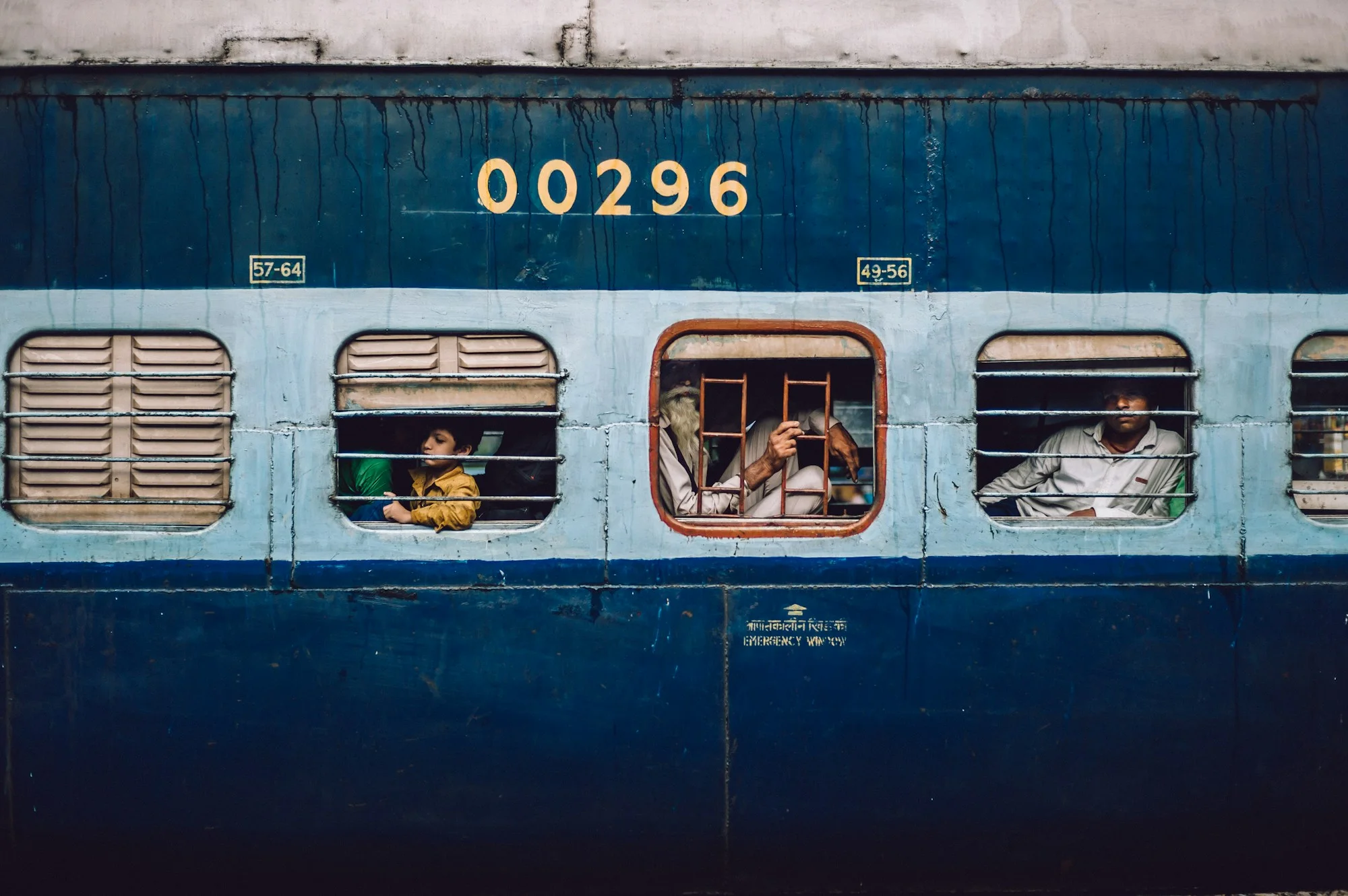 Passengers looking out of the windows of a blue Indian railway coach